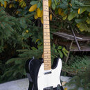 Černá elektrická kytara typu Telecaster s bílým pickguardem a světle hnědým javorovým hnedkem. Na hlavě kytary je viditelné oválné logo, které je vša…