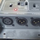 Šedý elektronický přístroj s nápisy INPUT, OUTPUT B a OUTPUT A nad odpovídajícími XLR konektory. Na horním panelu jsou přepínače LIFT a PAD s označen…