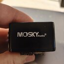 Černý obdélníkový modul s nápisem MOSKYAudio®. Na spodní straně je vidět kovový hřebenkový kontakt. Povrch je hladký s drobnými nečistotami.