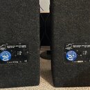 Dvě černé reproduktorové bedny potažené texturovaným materiálem. Na zadní straně každé bedny je štítek s nápisem PROFESSIONAL SPEAKER CABINET TYPE: S…