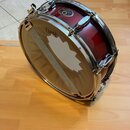 Červený buben s kovovými obručmi a úchytky. Na horním obruči je vidět logo TAMA, na korpusu je čitelný nápis Starclassic. Povrch nástroje vykazuje mí…