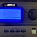Detail ovládacího panelu klavíru značky YAMAHA s modrým podsvíceným displejem, na kterém je nápis MidiGrand a grafické znázornění klaviatury. Pod dis…