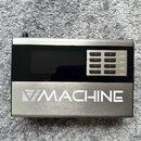 Kovové zařízení stříbrné barvy s černým displejem. Na spodní části je bílý nápis MACHINE s logem ve tvaru trojúhelníku. V pravé části jsou čtyři řady…