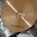 Zlatavý kovový činel s viditelným obráceným broušením povrchu. Na spodní části je černý nápis istanbul Agop Handmade cymbals from Turkey. V centru ci…