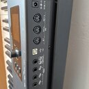 Detail zadní strany klaviatury s ovládacími prvky a konektory. Jsou zde viditelné nápisy: 9V DC / 1A, OUT 2 ↓, MIDI OUT 1 ↓, IN ↑, USB a PEDALS s čís…