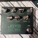 Tmavě zelený kytarový efekt s nápisem JOYO TIDAL WAVE. Na horní straně jsou čtyři chromované ovratovky s popisky LEVEL, BLEND, PRESENCE a DRIVE. Ve s…