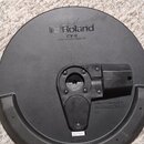 Kruhové černé gumové cymbalové pad s nápisem Roland a označením modelu CY-8 DUAL TRIGGER CYMBAL PAD. Uprostřed je umístěn černý plastový mechanismus…