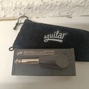 Černý textilní vak s bílým logem aguilar. Pod ním je šedá krabička s nápisy: aguilar, Model No. AP1-TU, MADE IN VIETNAM a dalšími texty v angličtině…