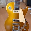 Zlatá elektrická kytara s jednodrážkovým tělem a bílým plechtrzem. Nástroj je vybaven dvěma humbuckery, chromovaným mostem s tremolo páčkou a čtyřmi…