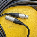 Černý audio kabel s dvěma stříbrnými konektory typu XLR. Na jednom z konektorů je viditelný nápis NEUTRIK. Povrch kovových částí vykazuje drobné škrá…