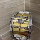 Zlatý kovový buben s chromovaným obručováním a ladicími šrouby. Na mechanismu v horní části je viditelný nápis "SONOR". Povrch nástroje je lesklý a b…