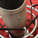 Stříbrný kondenzátorový mikrofon s černou mřížkou, umístěný v odpružíní. Na těle je vyrytý nápis CL7 STUDIO CONDENSER a viditelné kulaté tlačítko. Po…