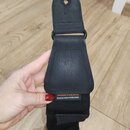 Černý popruh na hudební nástroj z kombinace textilu a syntetického materiálu s texturou kůže. Na spodní části koženého elementu je bílý nápis Designe…