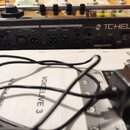Zadávací panel černého zařízení s nápisem TC HELICON. Jsou zde viditelné vstupy a výstupy označené jako MIC/LINE, GUITAR, MONITOR, VOICE L (MONO) a R…