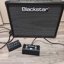 Černý kytarový kombo zesilovač s bílým logem Blackstar na přední mřížce. Před ním leží černý dvoupedálový spínací jednotka s nápisy Blackstar, CHANGE…
