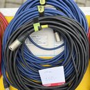 Na fotografii jsou dva svinuté kabely, jeden modrý a druhý černý. Černý kabel má na povrchu nápis MICROPHONE CABLE HIGH PERFORMANCE a je označen papí…