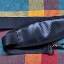 Černý popruh na hudební nástroj z textilu a syntetického materiálu s karbonovou strukturou v středové části. Na koncích jsou kovové karabiny a nastav…