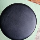 Fotografie zachycuje horní část kulatého sedáku potaženého černým materiálem s texturou kůže. Povrch je v dobrém stavu bez viditelných poškození. Na…