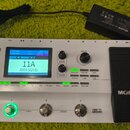 Bílý kytarový procesor s černým pedálem zprava. Na přístroji je nápis VGE 250 Amp Modeling & Multi Effects a na pedálu značka MOOER. Displej zobrazuj…