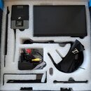 V bílém polystyrenovém packingu v krabici je umístěna sada bezdrátového systému. Je zde černý přijímač s nápisem XS WIRELESS SENNHEISER a logo značky…