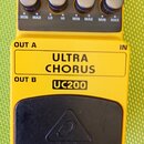 Žlutý kytarový efekt s černým ovládacím panelem a černým spínacím pedálem. Na šasi jsou nápisy ULTRA CHORUS a UC200, na pedálu je logo behringer. Hor…