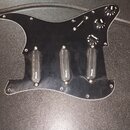 Černý plastový pickguard pro kytaru s třemi černými snímači. Na každém ze snímačů je bílý nápis "Wilkinson". Součástí jsou tři černé ovládací knofíky…
