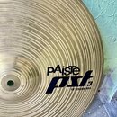 Zlatý kovový činel s koncentrickými rýhami. Na povrchu je černý nápis pAiste a pod ním stylizované logo pst 3 s doplňkem 18" CRASH RIDE. Povrch je či…