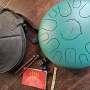 Zelený steel tongue drum s vyrytými čísly 1 až 10 a centrálním logem LENA v ornamentálním kruhu. K nástroji patří černý přepravní vak, dva dřevěné pa…