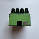 Zelený kytarový efekt s čtyřmi černými ovládacími knoflíky. Na zadní straně je vstup pro napájení a štítek s nápisem USE BOSS ACA ADAPTOR ONLY. Povrc…