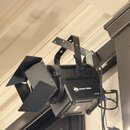 Černý světelný reflektor s nastavitelnými klapkami, který je připevněn na kovový držák. Na boku přístroje je bílý nápis ADJ ENCORE FRISO2 a symbol CE…