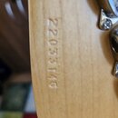Detail zadní strany hlavy kytary z přírodního dřeva. Na povrchu je vyrazeno sériové číslo 22033146. V pravé části jsou vidět kovové ladičky.