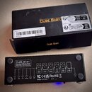 Fotografie zobrazuje černý efektový pedál s nápisem CUBE BABY Combined Effects Pedal a jeho originální černé balení. Na zadní straně pedálu jsou vidi…