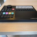 Černý sekvencer Polyend Tracker + s displejem, ovládacím knoflem a mřížkou bílých tlačítek. Na pravém boku je nápis Polyend Tracker +. Na zadní stran…