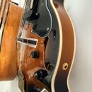 Detail polodublové elektrické kytary v barevně sunburst. Nástroj má černý plechový pickguard, dva černé ovládací knofíky a zlatý mostek. Na těle není…