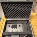 Stříbrný kytarový procesor s nápisem AMPERO a podtitulem Guitar Processor v černé tlumící pěnové kufře. Na pravém boku zařízení je oranžový nápis HOT…