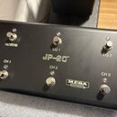 Černý kovový spínací pedalboard s šesti stoupacími spínači. Uprostřed je bílý nápis JP-2C™, v dolní části pravy doprava logo MESA ENGINEERING. Spínač…