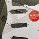 Bílá plastová pickguard pro elektrickou kytaru s několika otvory na šrouby a výřezy. Na ní leží průhledná plastová pravítko s měřítkem v palcích. V p…