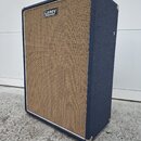 Kytarový reproduktor v modrém potahu s hnědou pletenou mřížkou. V horní části mřížky je umístěno bílé obdélníkové logo s nápisem Laney. Rohy skříně j…