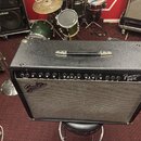 Černý kytarový kombo zesilovač s látkovou maskou reproduktorů. Na předním panelu je nápis Frontman 212R a logo Fender. Ovládací panel obsahuje několi…