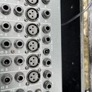 Detail zadní strany šedého audio zařízení s řadou vstupů a výstupů. Jsou zde viditelné konektory typu XLR, jack a cinch s popisky jako INS, LINE, MIC…
