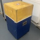 Modrý transportní case s žlutým horním víkem, vybavený kovovými hranami a úchyty. Na horní straně je vidět červenobílá zakázková značka s přeškrtnutý…