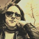 Na fotografii je portrét osoby v slunečních brýlích, kožené bundě a pleteném svetru. Fotografie nemá vztah k hudebním nástrojům ani příslušenství.