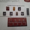 Fotografie zobrazuje schéma zapojení kytarového efektového pedalboardu. V centru je červený přístroj s nápisem OCTA-SWITCH MK3, na kterém jsou vidět…