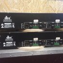 Dvě černé rackové jednotky značky dbx PROFESSIONAL PRODUCTS naskládané na sebe. Na zadní stranách jsou viditelné vstupy a výstupy, včetně konektorů X…