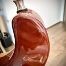 Detailní záběr na horní část těla hnědého lakovaného nástroje, pravděpodobně kytary. V horní části je vidět kovový kolík s černou plstěnou podložkou.…