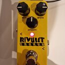 Žlutý kytarový efekt s nápisem RIVULET CHORUS. Na horní straně jsou tři černé otočné knoflíky s popisky RATE, WIDTH a INTENSITY. Uprostřed svítí růžo…