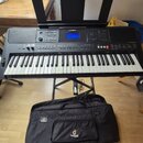 Černý digitální klavír značky YAMAHA, model PSR-E453, umístěný na černém X-stojanu. Nástroj má bílé a černé klávesy, displej a ovládací tlačítka. Pře…