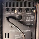 Zadní strana zesilovače s kovovým šedým panelem. Jsou zde viditelné nápisy SPEAKERS, POWER AMP 2, BRIDGE a POWER AMP 1, spolu s přepínači a konektory…