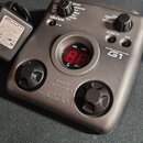 Šedý kytarový efekt pedál s nápisem GUITAR EFFECTS PEDAL G1 a logem ZOOM. Zařízení má dvě stoupací pedály, několik ovládacích knoflíků a červený digi…