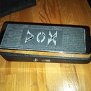 Černý kompaktní zesilovač s kovovým vrškem a texturovaným spodním tělem. Na horní straně je vyfrézovaný nápis AMPLIFIER a výrazné logo VOX. Povrch vy…